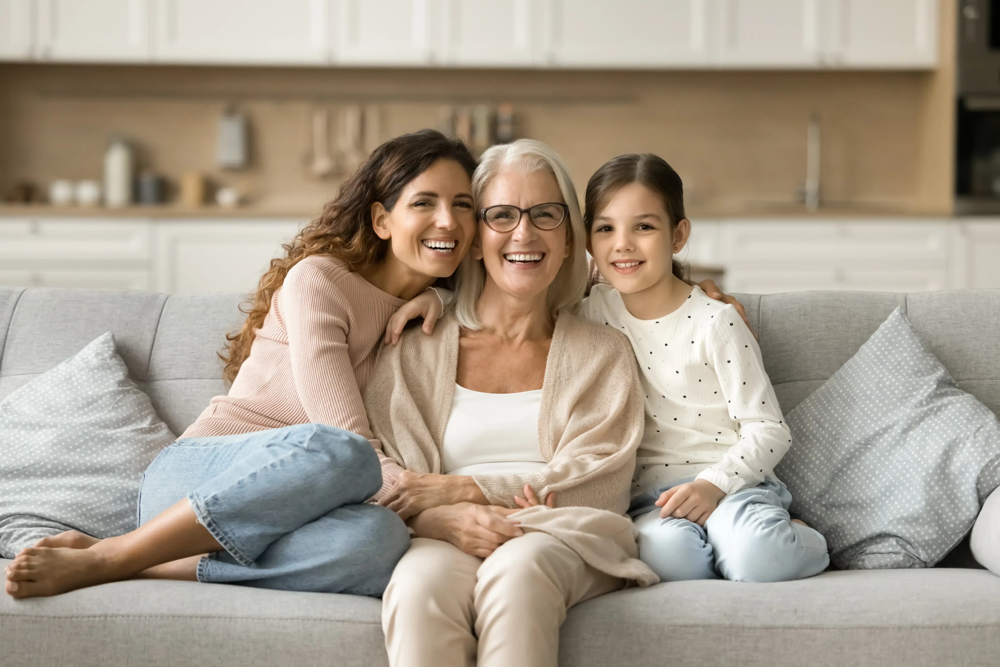 Avó, mãe e filha sentadas em um sofá, sorrindo com tranquilidade após terem conquistado benefício no INSS.