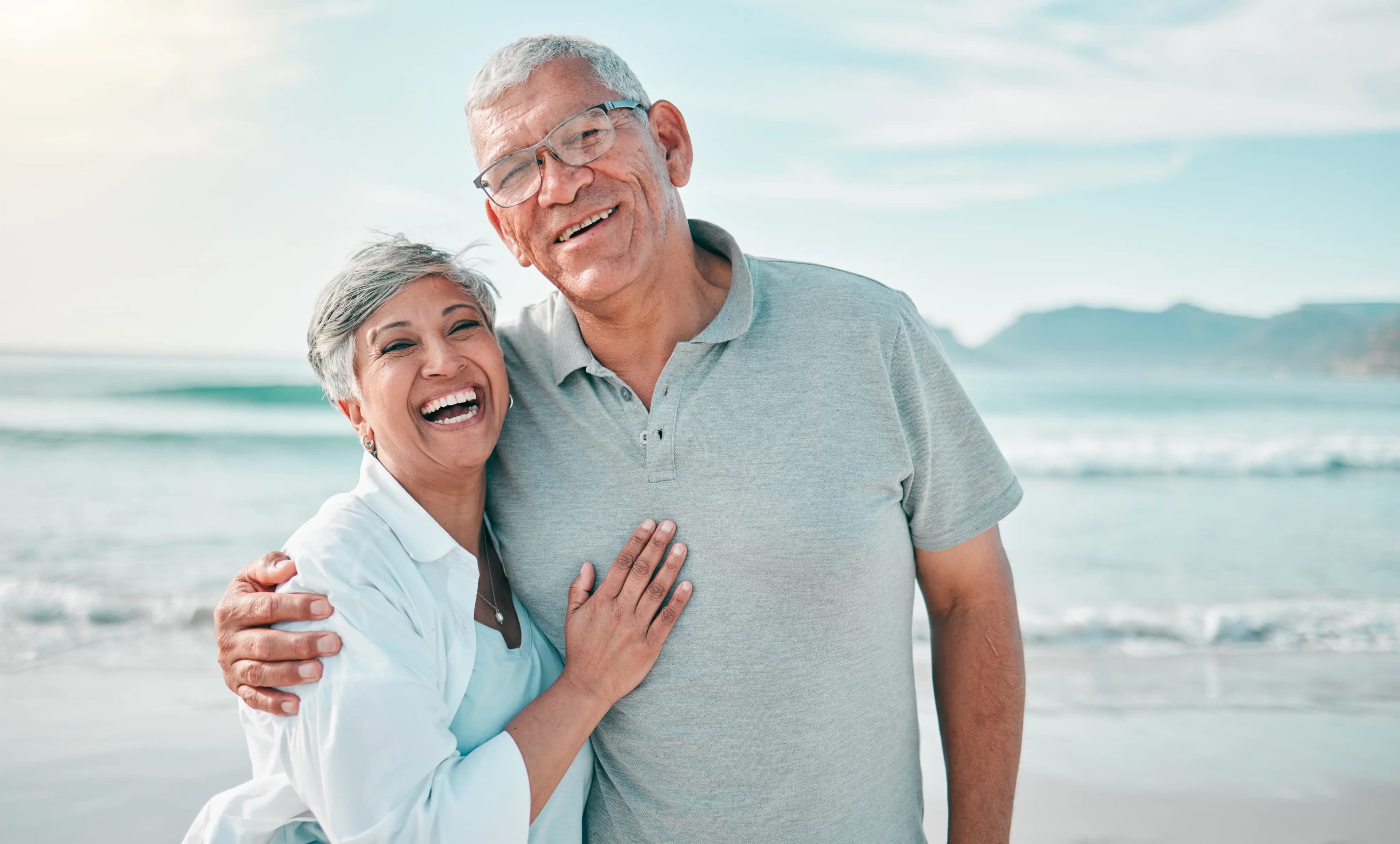 Casal de brasileiros que conseguiram sua aposentadoria do INSS. Estão na praia, sorrindo.